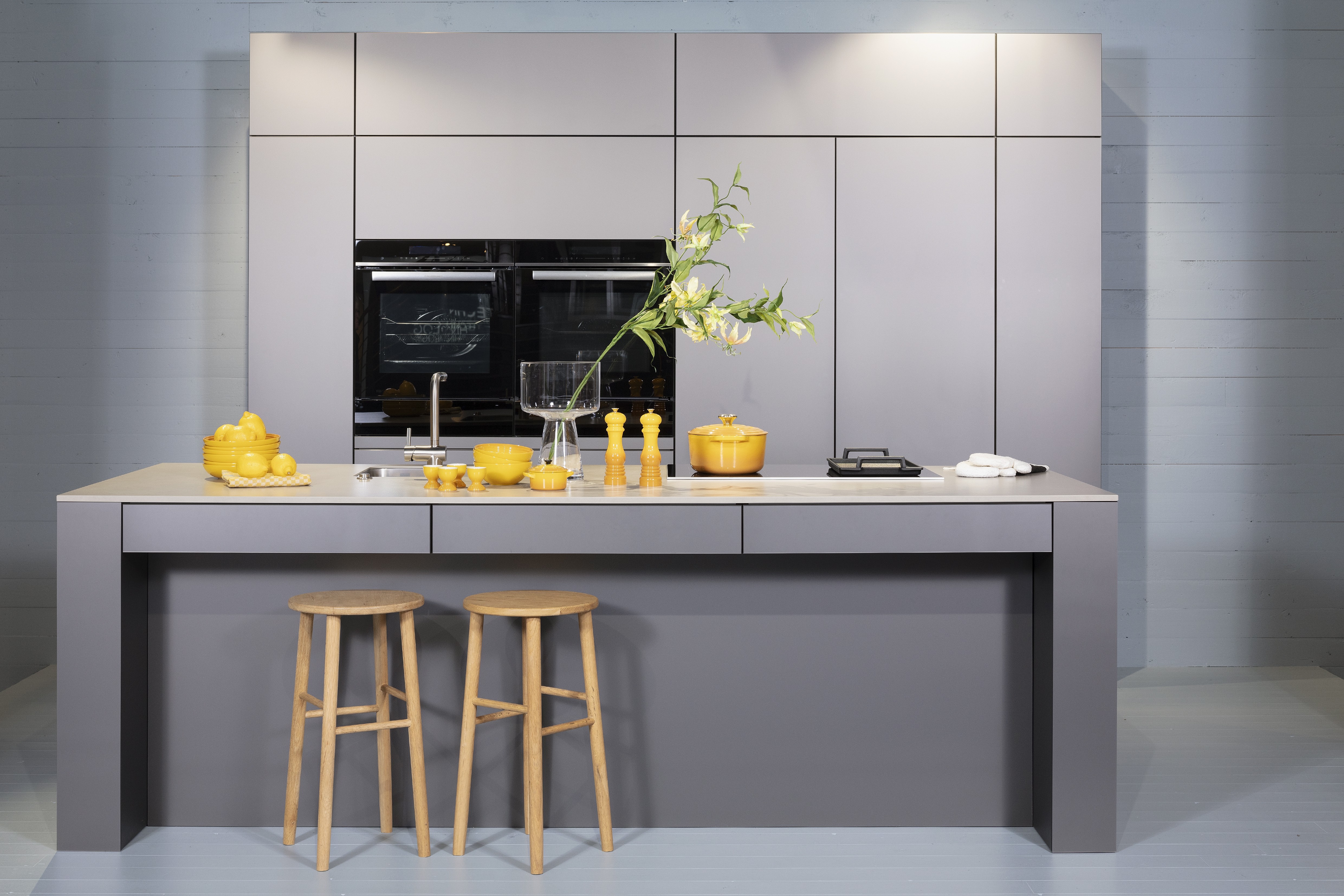 Concept130ART Front: SMART-GL Sandgrau metallic APL: SMART-GL Carbon metallic Geräte Blaupunkt Armatur und Spüle: Franke  Features: Insellösung mit Thekenfunktion mit Schubladen, Teppanyakiaufsatz für Kochfeld, Schubladen in Silber, Schubladen mit Griffmulde, Nischenlösung in Blau mit Regalfunktion.