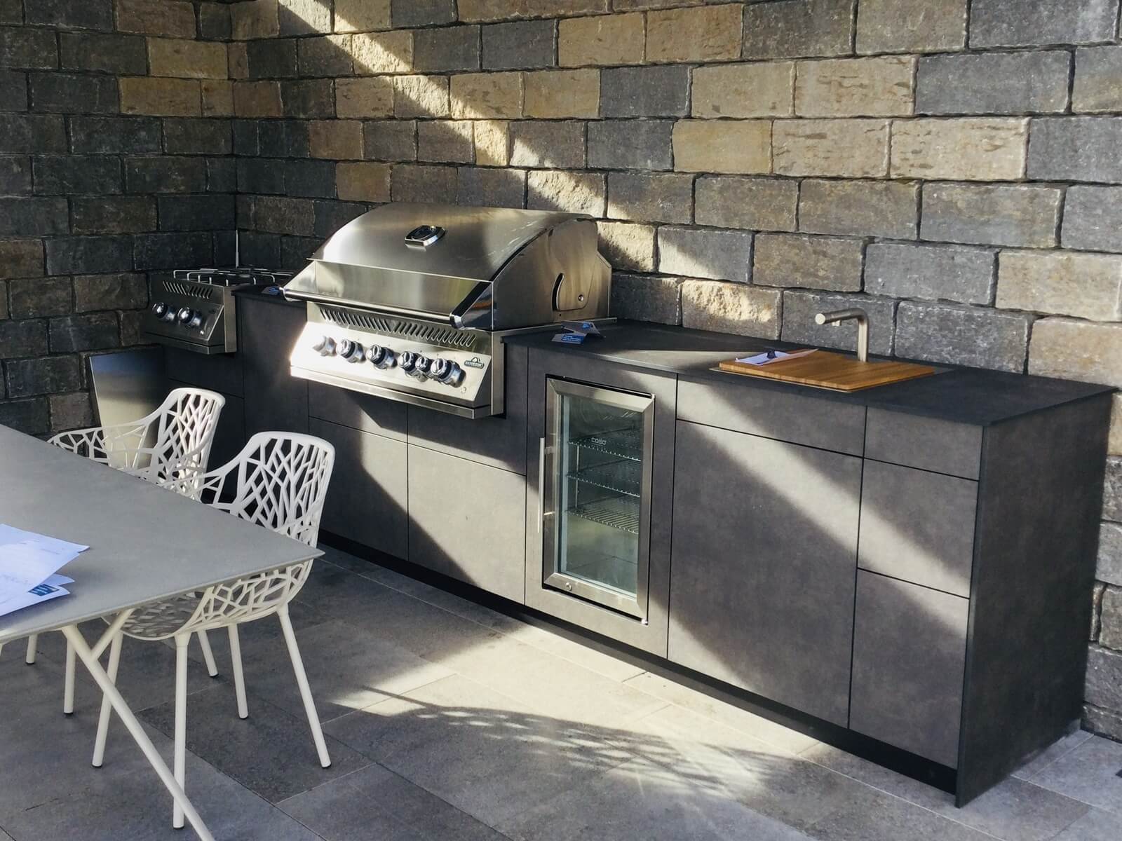 Küchenzeile mit Grill und Kühlschrank vor Mauerwerk mit Freilichteinfall