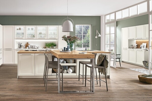 Weiße CASCADA 774 Landhausküche. Die Weiterführung des Dekors im Flur bringt ein einheitliches Gesamtbild. Tolle Ergänzung ist hier die Kücheninsel mit integriertem Tisch in Naturholz-Optik.