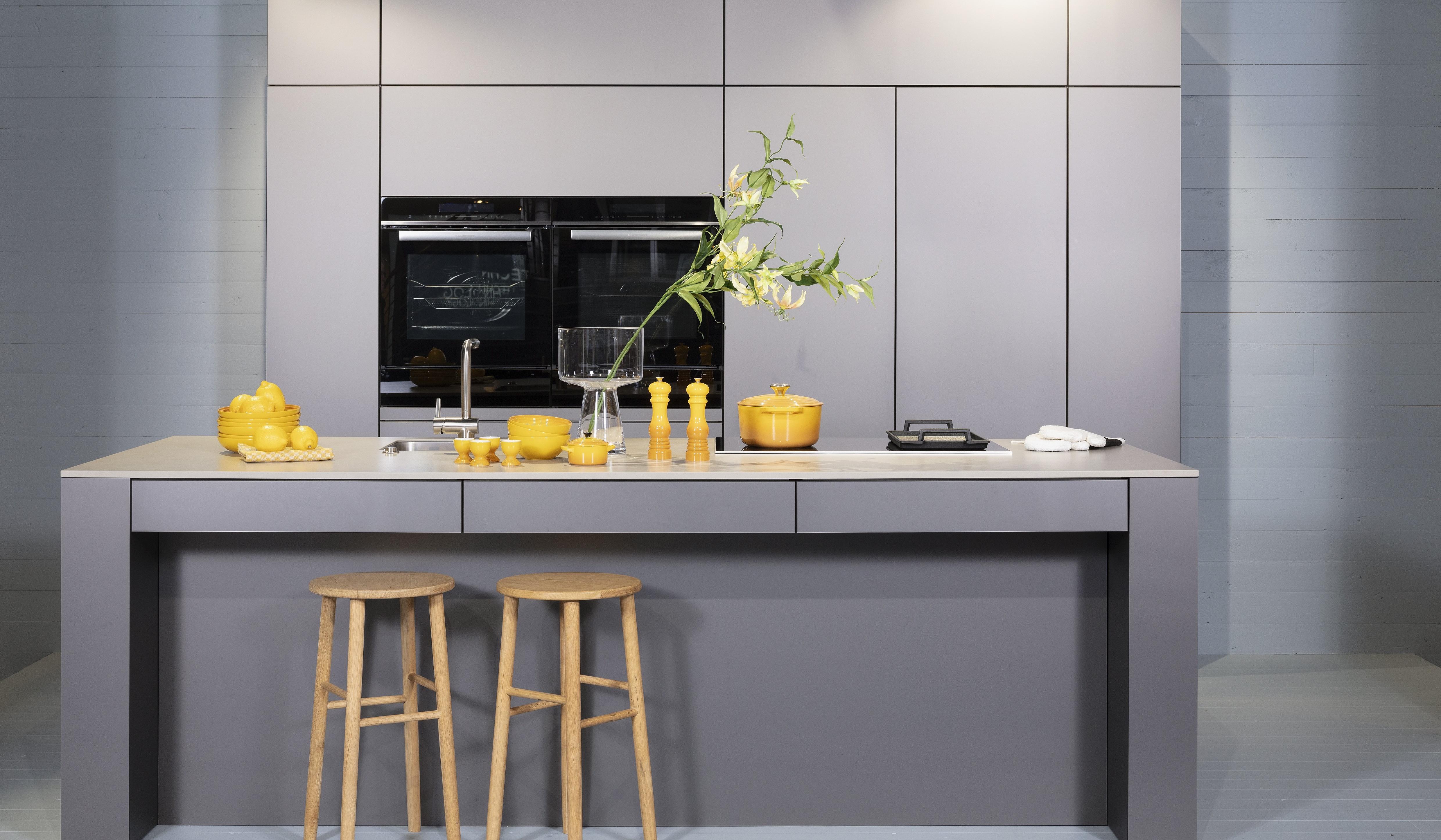 Concept130ART Front: SMART-GL Sandgrau metallic APL: SMART-GL Carbon metallic Geräte Blaupunkt Armatur und Spüle: Franke  Features: Insellösung mit Thekenfunktion mit Schubladen, Teppanyakiaufsatz für Kochfeld, Schubladen in Silber, Schubladen mit Griffmulde, Nischenlösung in Blau mit Regalfunktion.