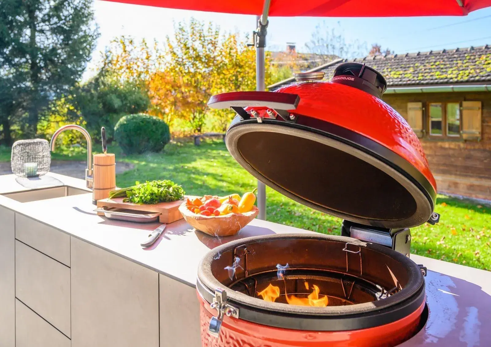 Küchenzeile im Garten mit geöffnetem rotem Grill-Ei